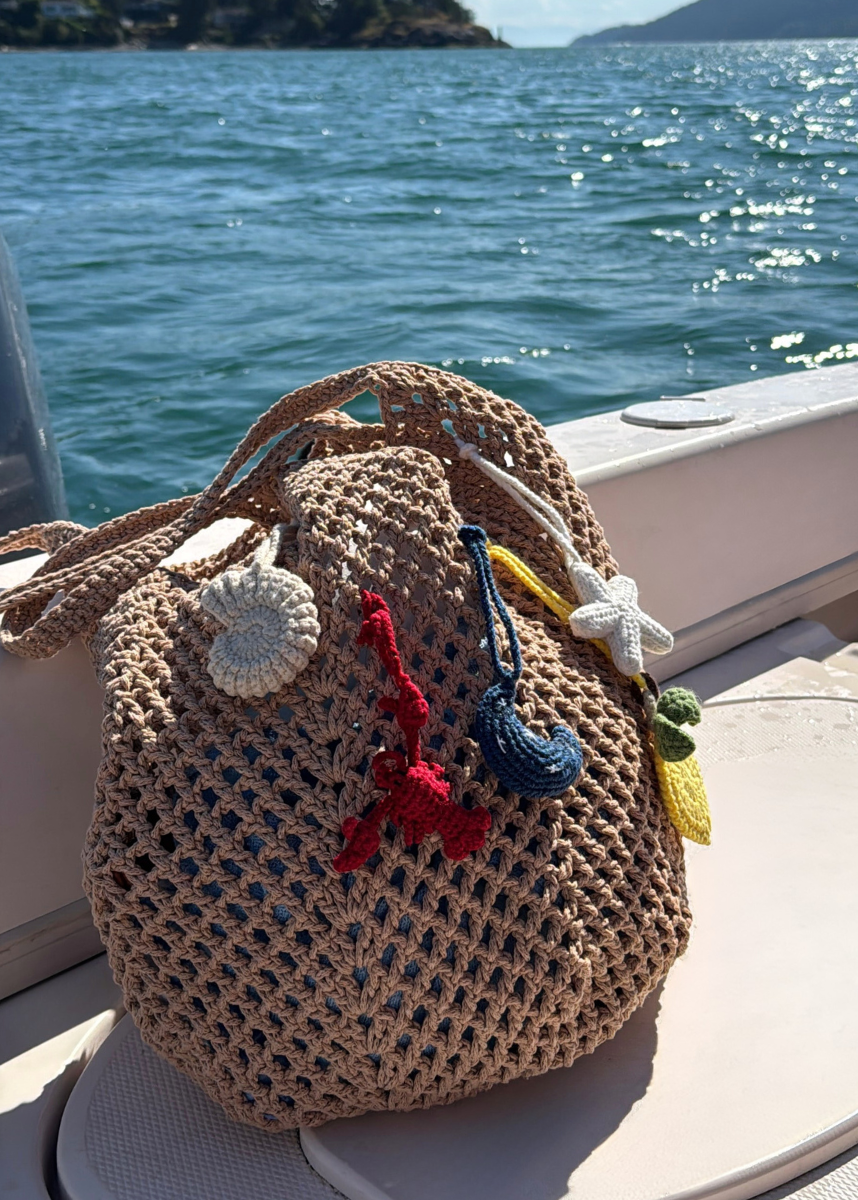Crocheted bag with colorful handmade bag charms on a boat with ocean background